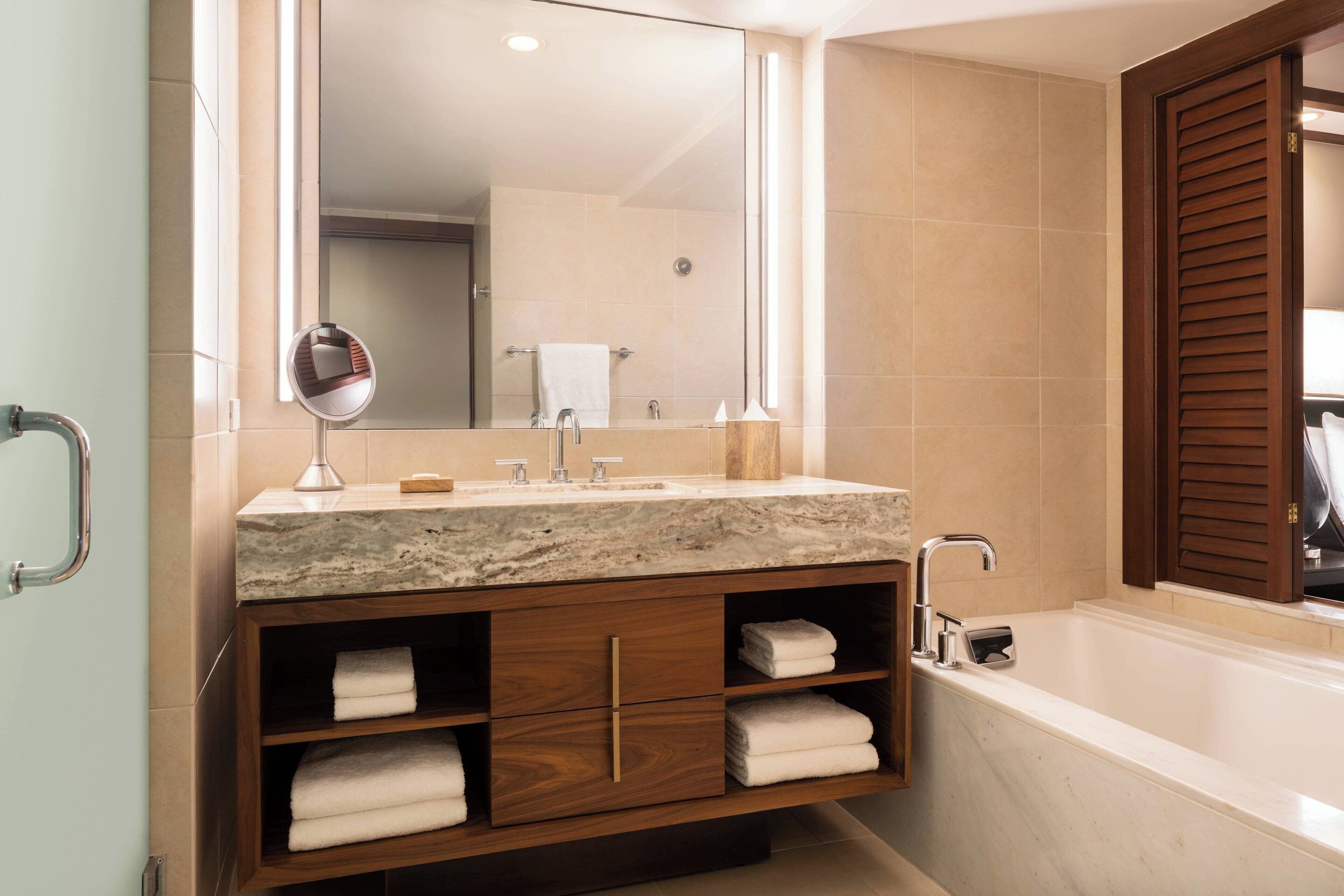 A modern bathroom with a marble sink, wooden vanity, and a large bathtub.
