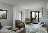 A modern living room with a large window, two wicker chairs, a hanging chair, and a view of the outdoors.