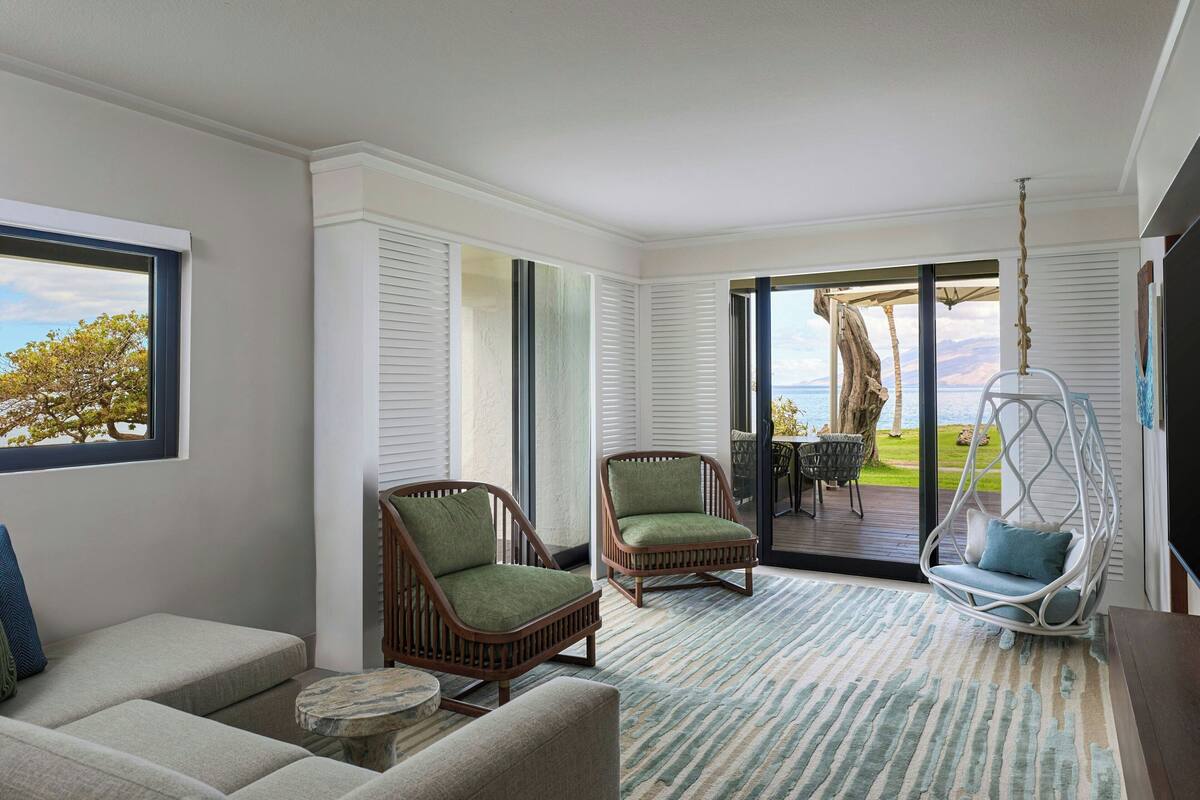 A modern living room with a large window, two wicker chairs, a hanging chair, and a view of the outdoors.