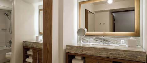 A modern bathroom with a marble vanity, wooden cabinetry, a large mirror, and a shower area.