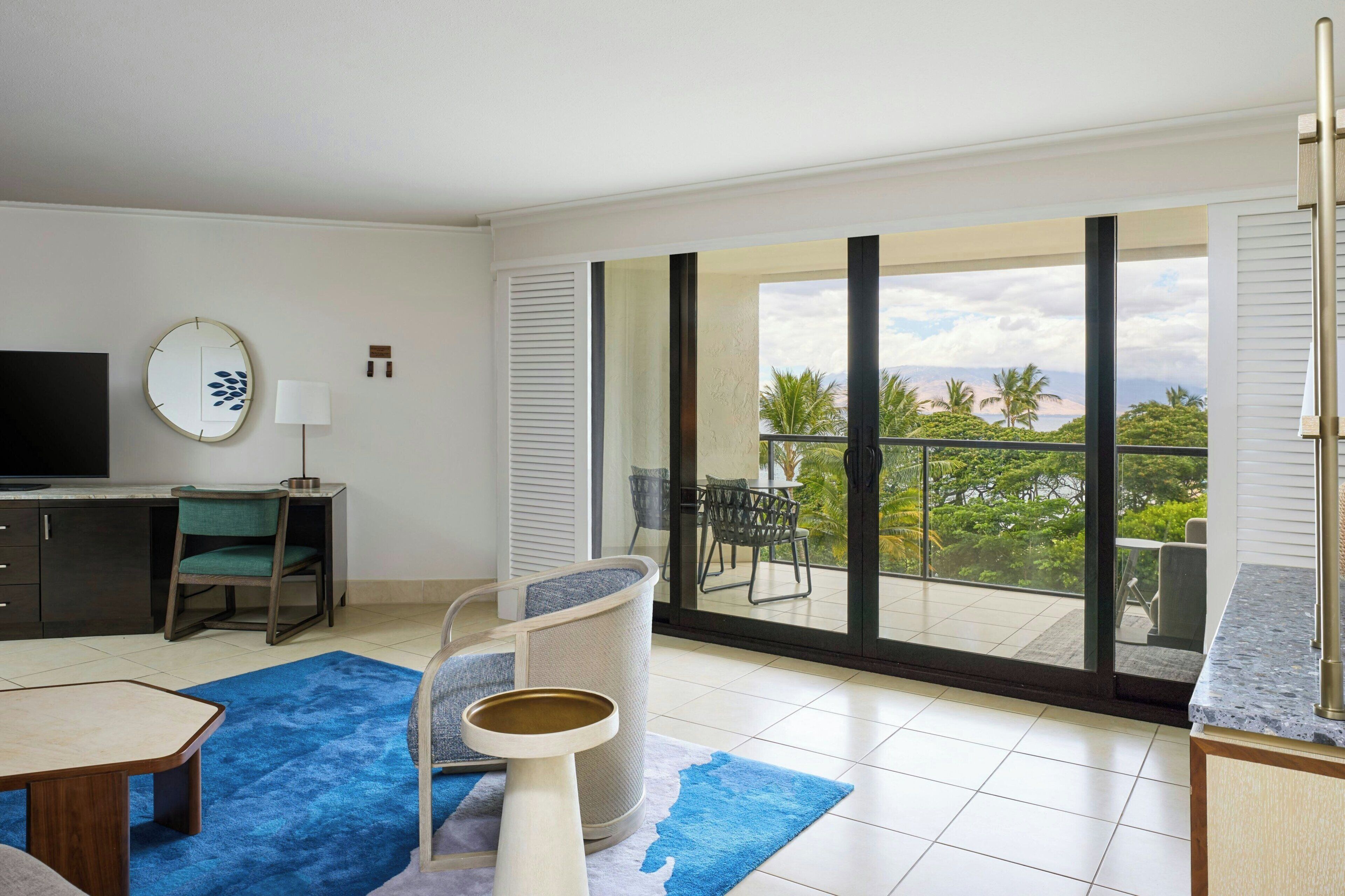 A modern hotel room with a balcony, a dining area, and a TV.