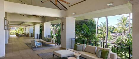 A spacious indoor area with a balcony overlooking palm trees, featuring a sofa, chairs, and a ceiling fan.