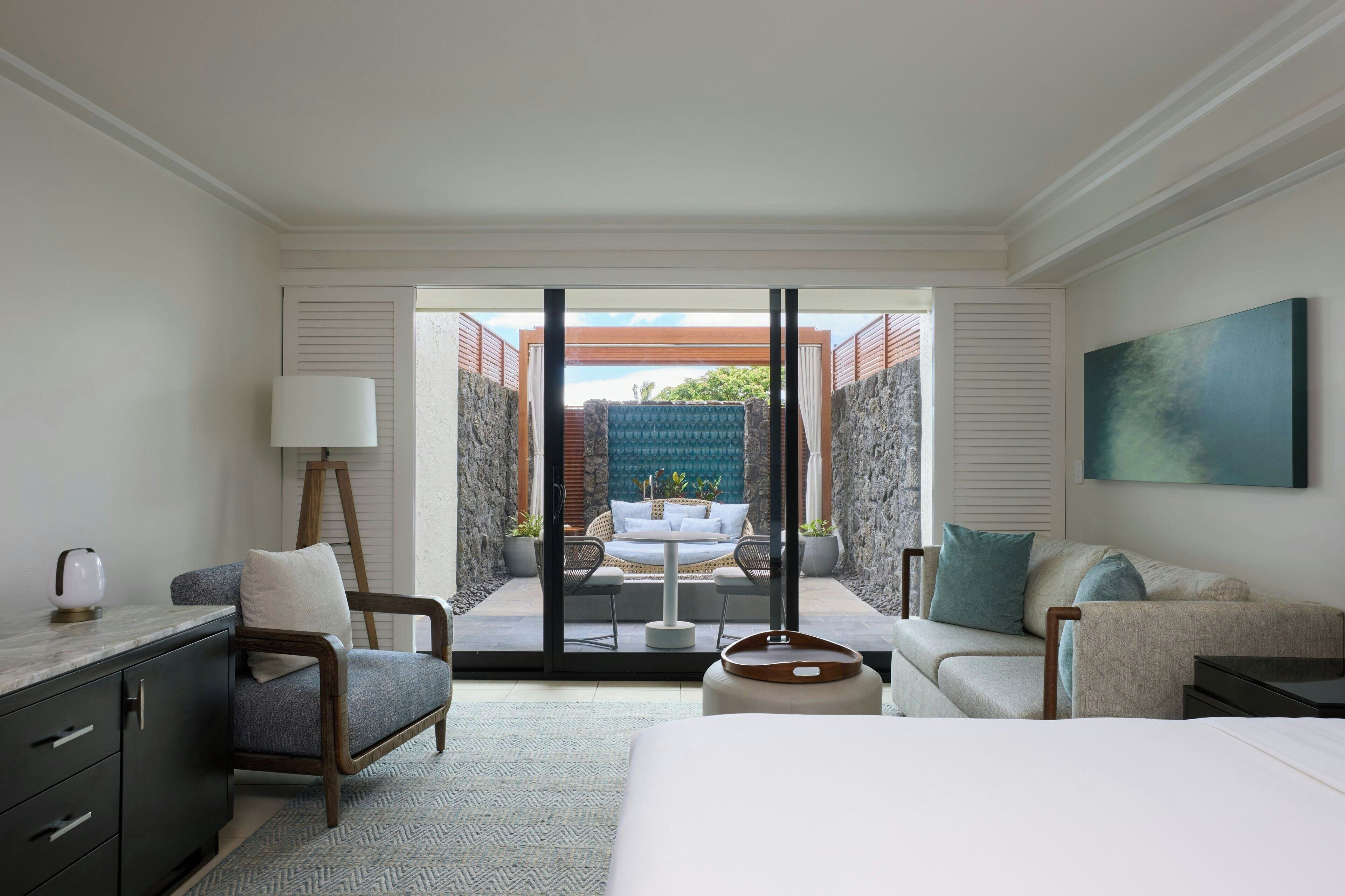 Habitación de hotel con cama, escritorio, sillón, sofá y balcón con vistas al exterior.
