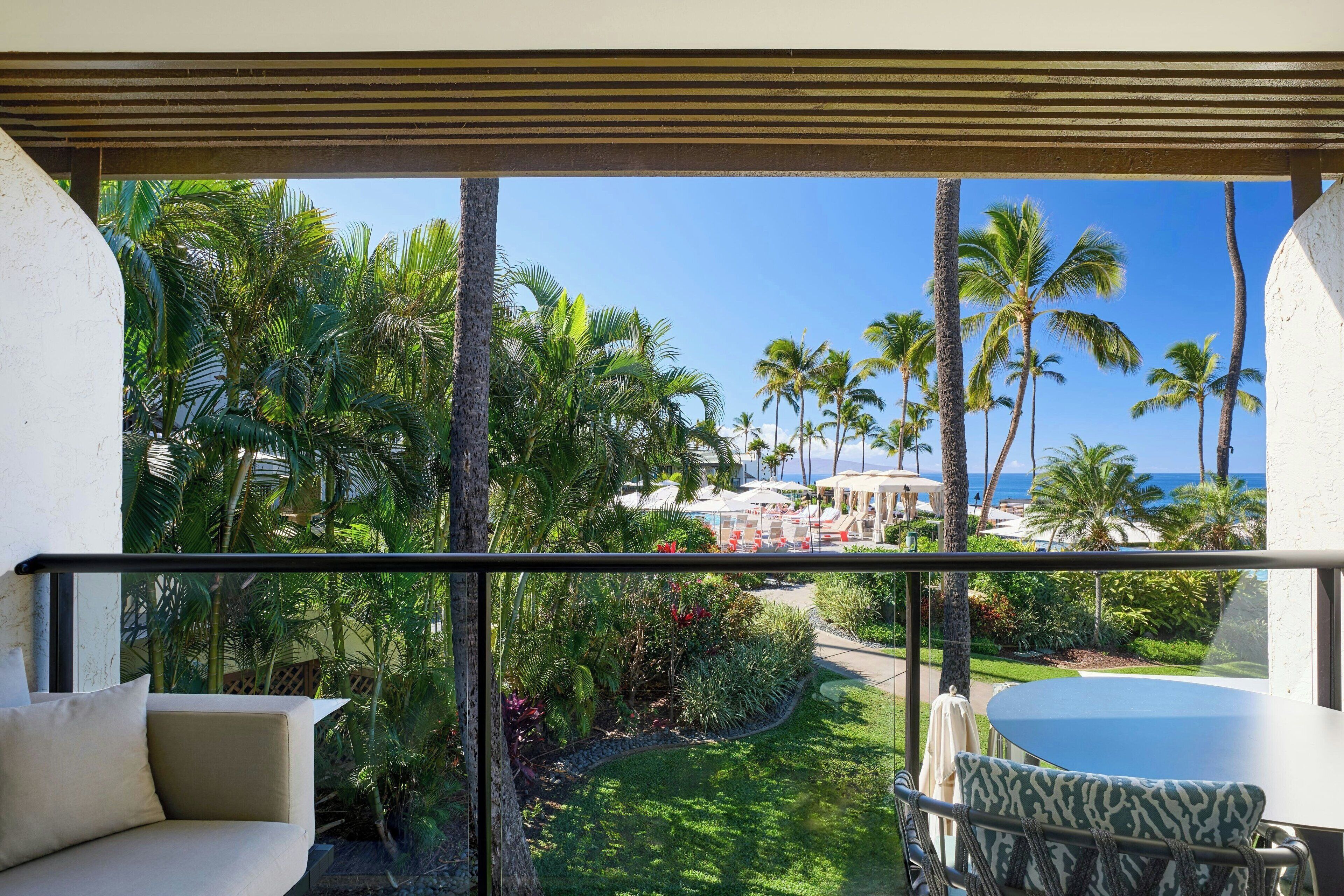 A balcony with a view of a tropical garden and the ocean.