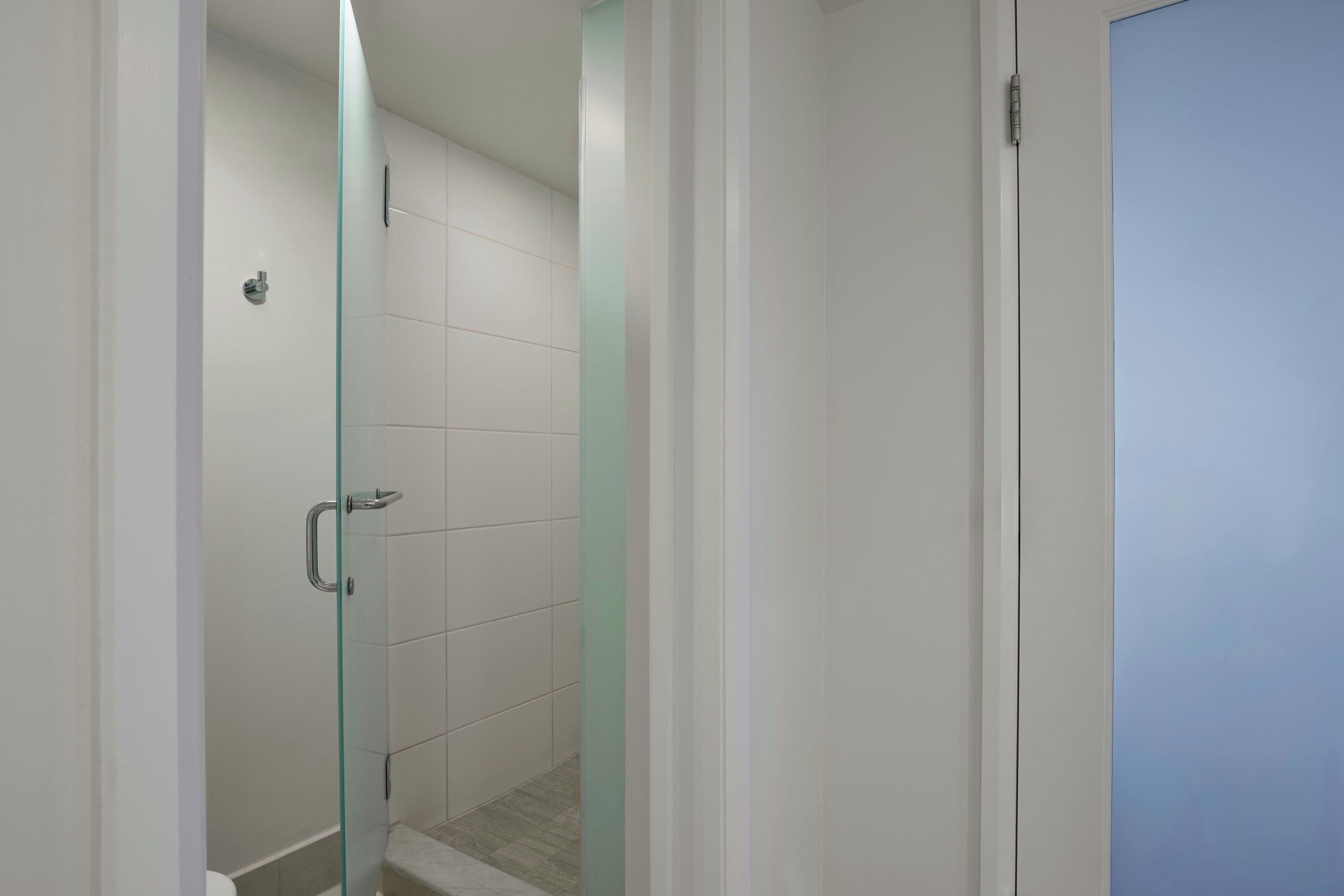 A bathroom with a glass shower enclosure, white tiled walls, and a door with a handle.