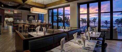 Un restaurant offrant une vue imprenable sur le coucher de soleil, avec des poutres en bois, de grandes fenêtres et un aménagement intérieur moderne.