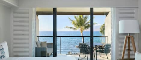 A hotel room with a large bed, a balcony with a table and chairs, and a view of the ocean.