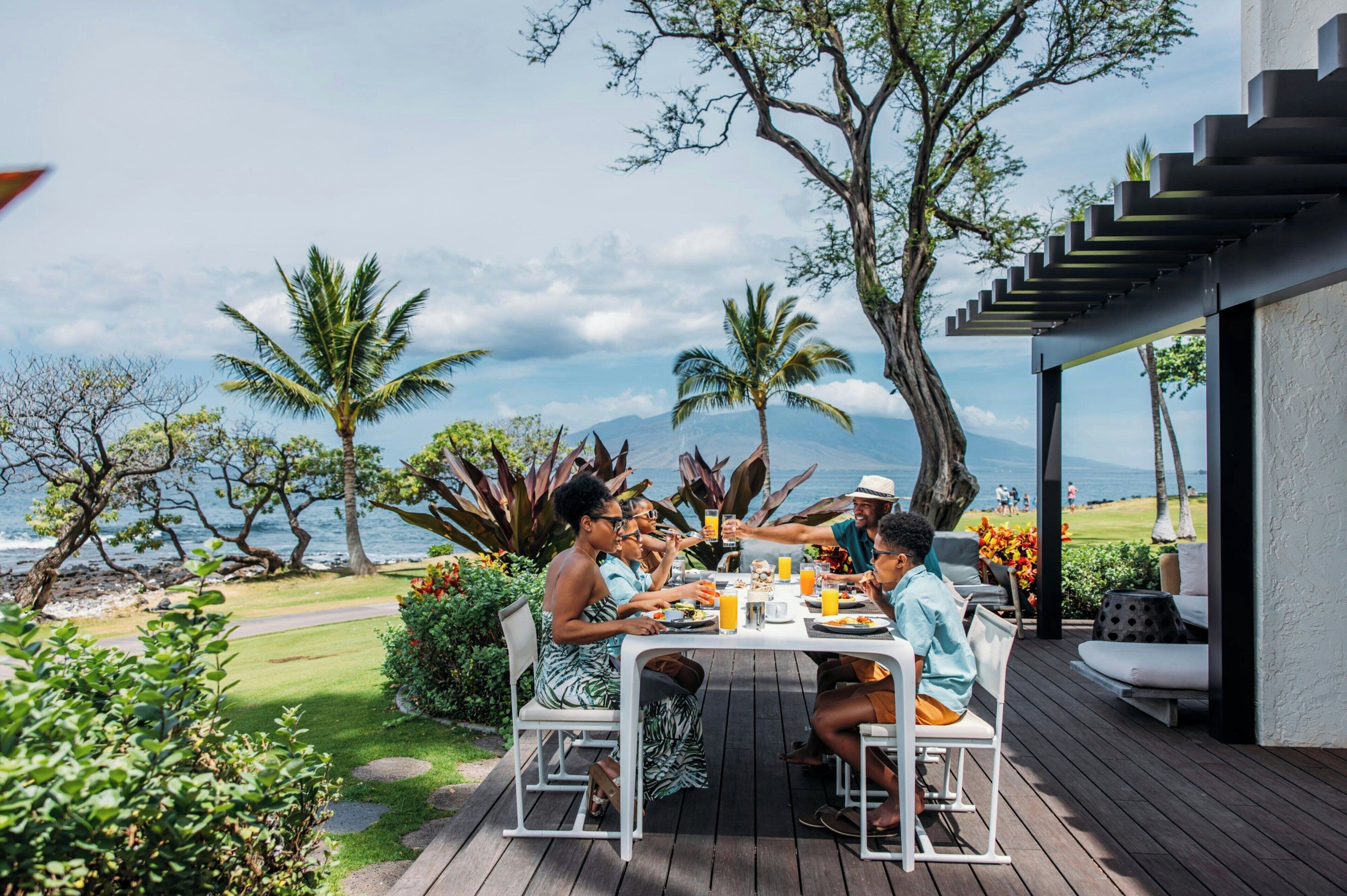 Un grupo de personas cenando al aire libre con vista al océano y montañas.