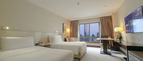 Habitación de hotel con dos camas, un escritorio con computadora, televisión y vista a la ciudad.