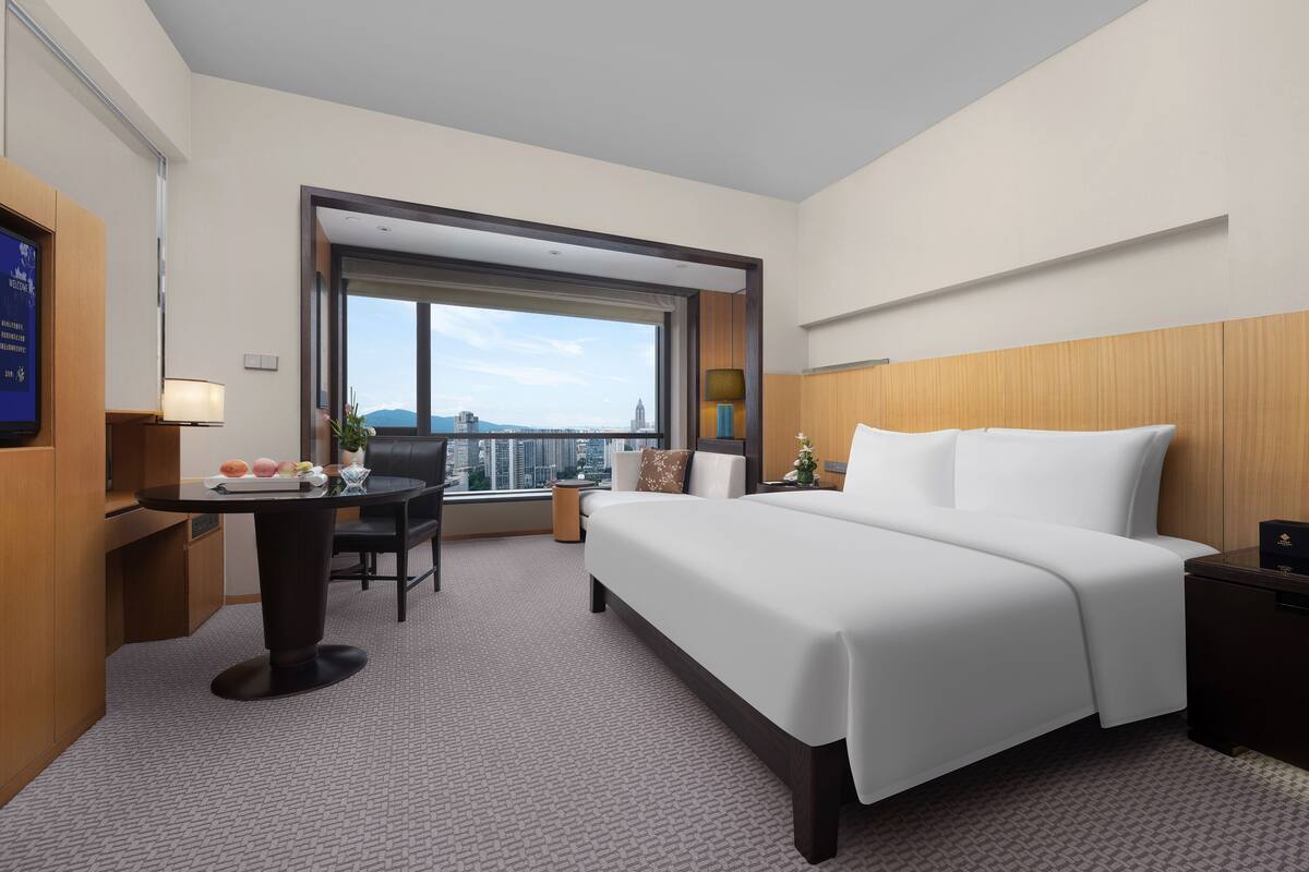 Une chambre d’hôtel avec un lit, un bureau, une chaise, une lampe et une vue sur la ville.