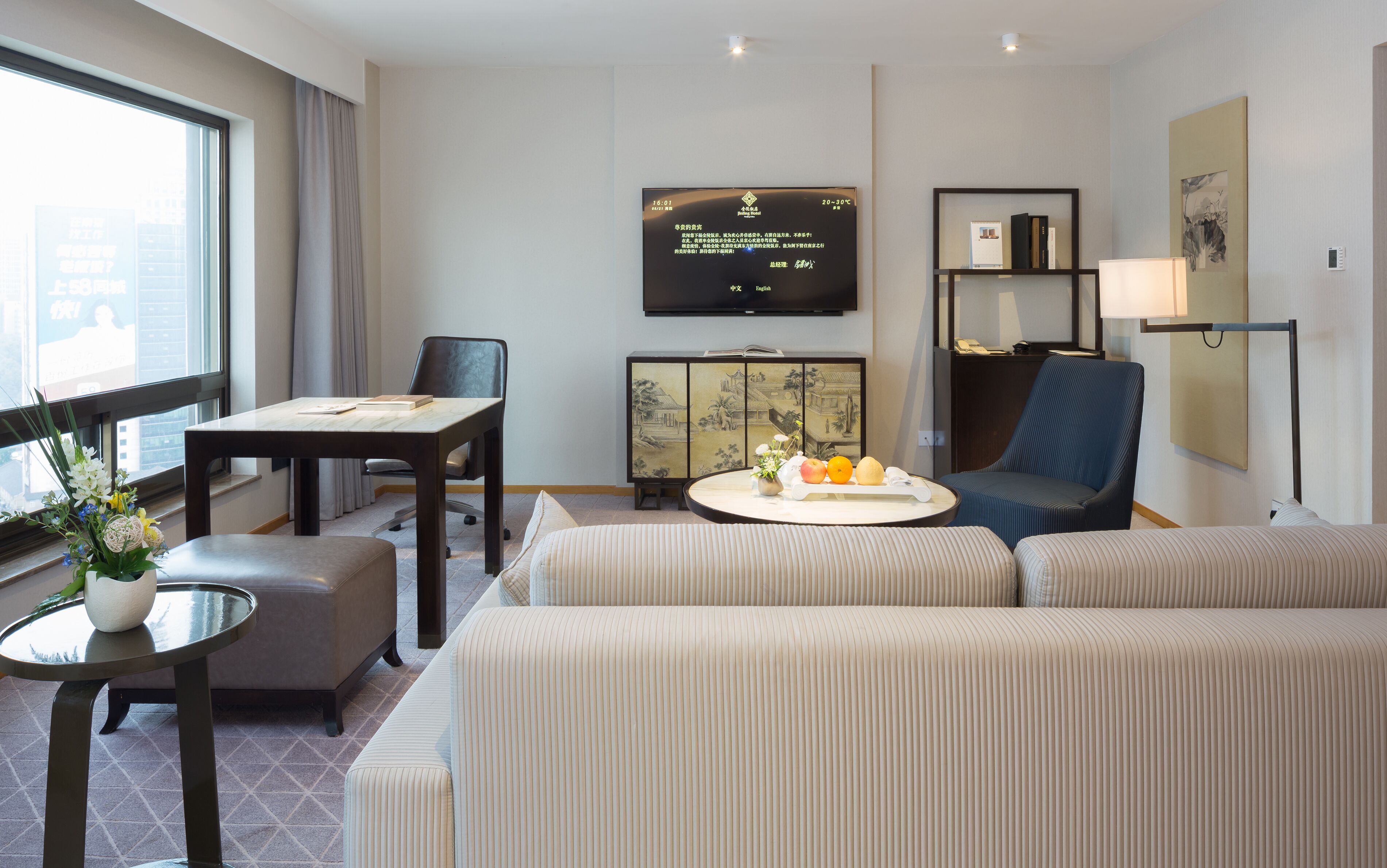 Una camera d'albergo con un divano, un tavolo da pranzo, una TV e un mobile contenente opere d'arte.