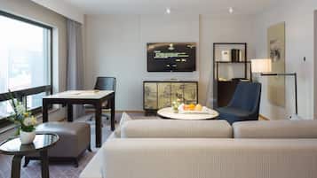Una camera d'albergo con un divano, un tavolo da pranzo, una TV e un mobile contenente opere d'arte.