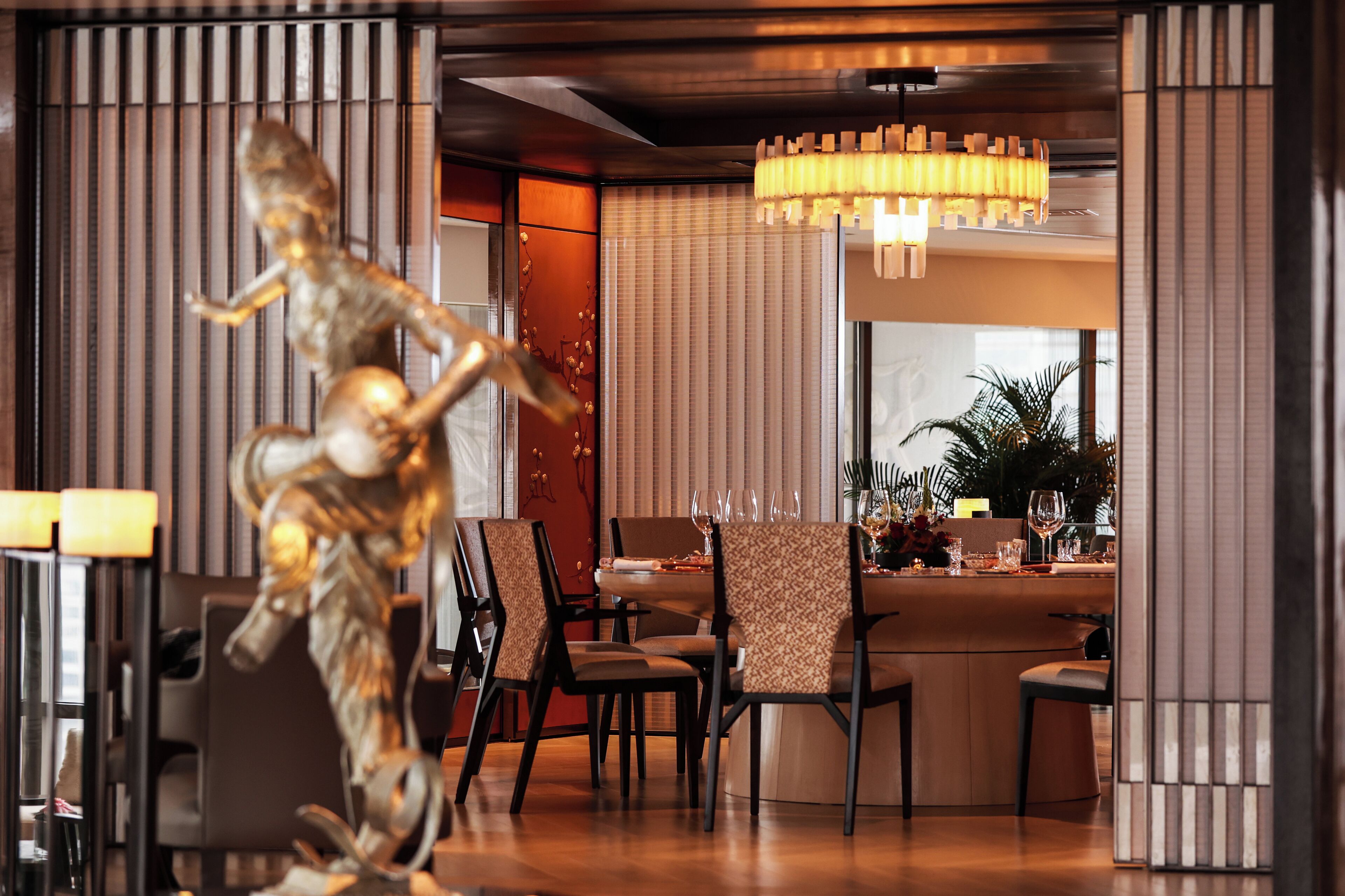 A modern dining area with a central round table, chairs, and a decorative sculpture.