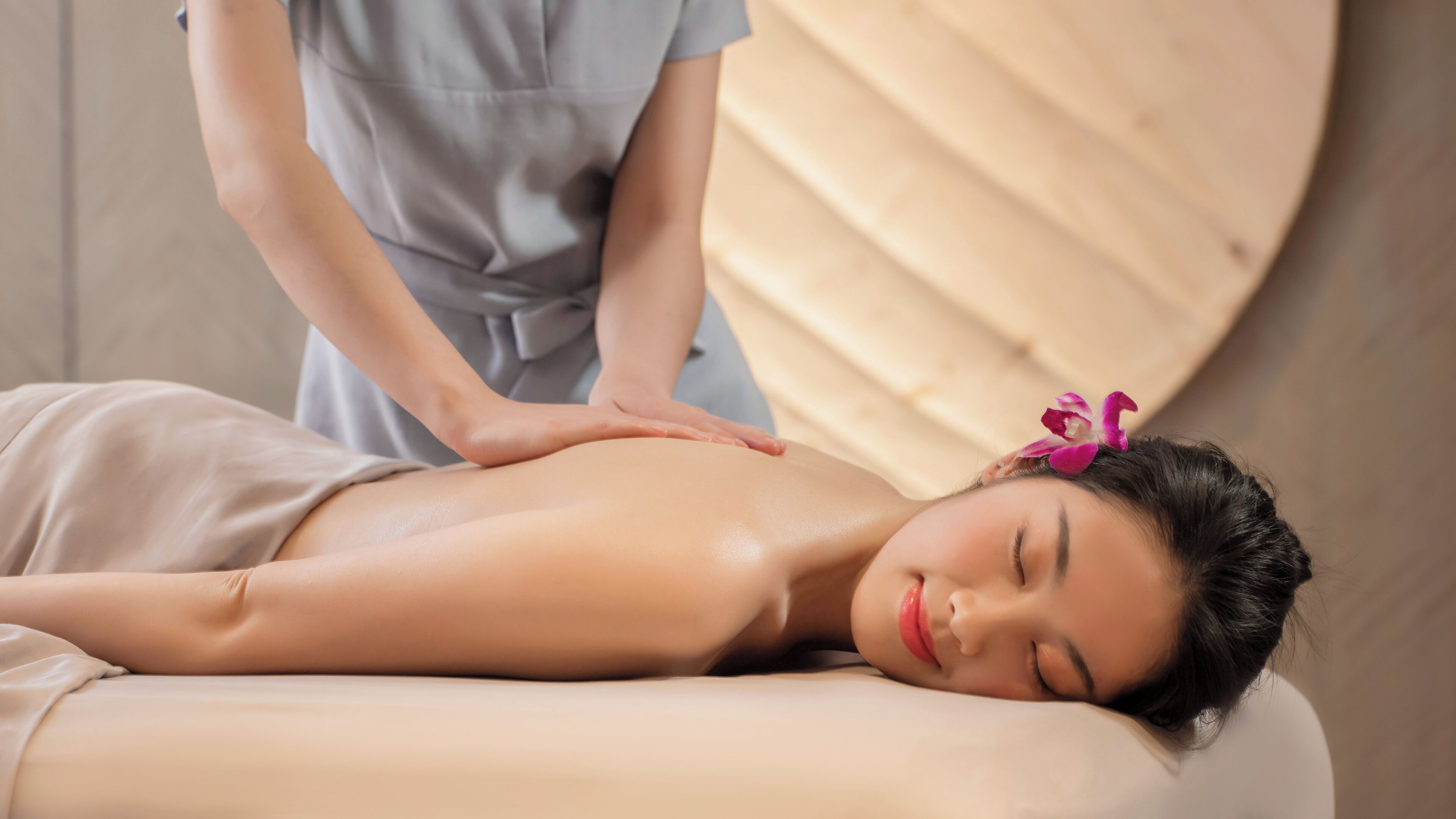 A person receiving a massage in a room with a wooden panel wall and a bed.