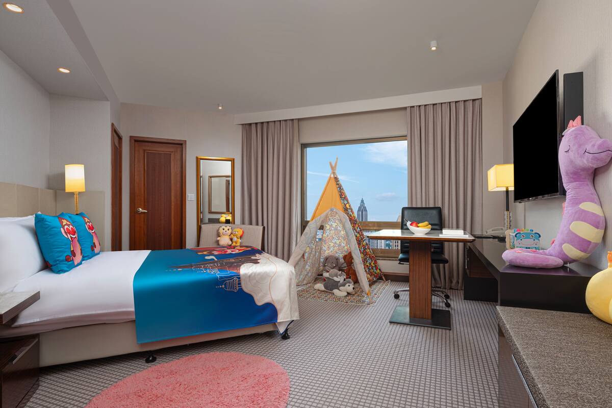 Une chambre d’hôtel équipée d’un lit, d’un bureau, d’une chaise, d’une télévision et d’une fenêtre donnant sur la ville.