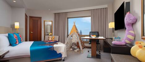 Habitación de hotel con cama, escritorio, silla, televisor y ventana con vista a la ciudad.