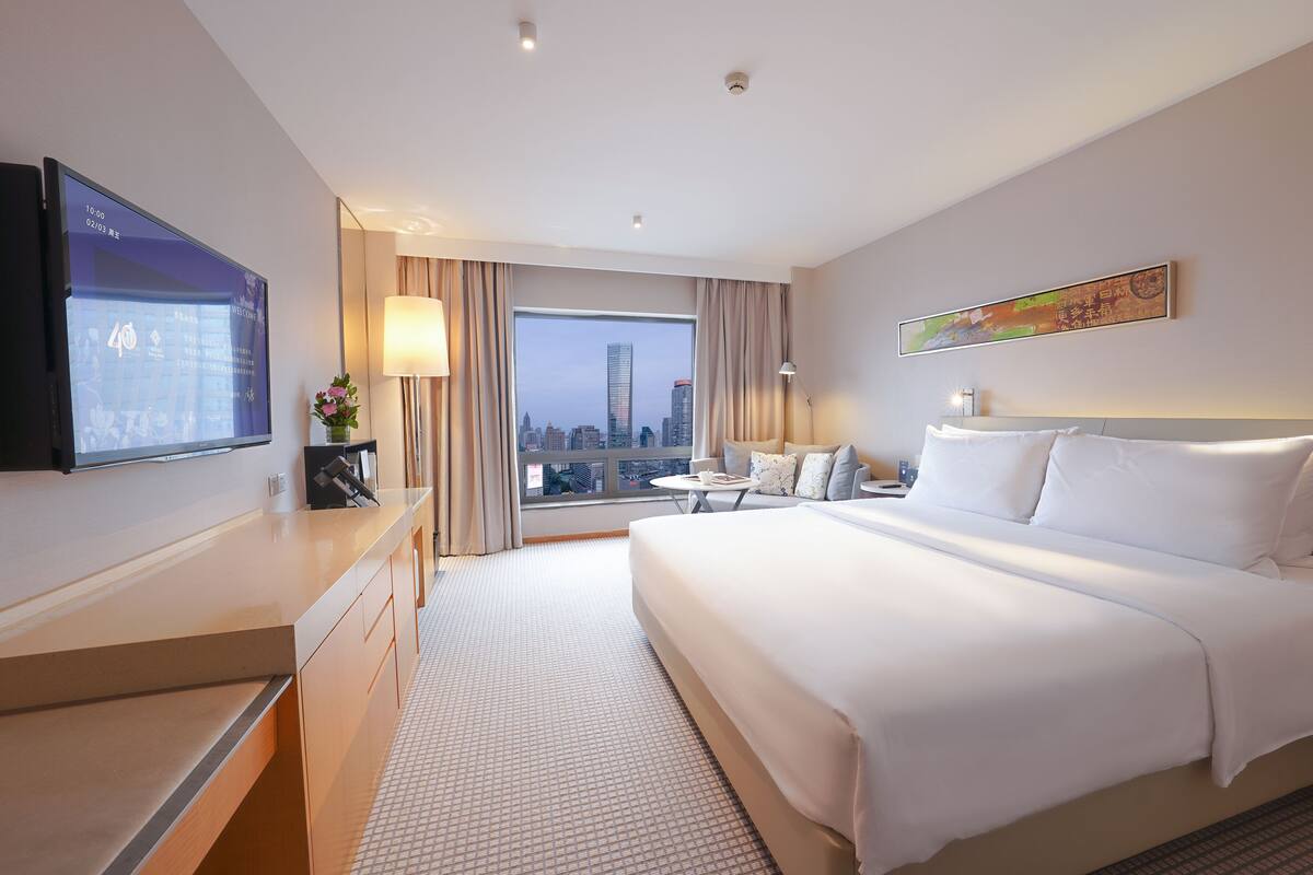 Une chambre d’hôtel moderne dotée d’un grand lit, d’un bureau, d’une télévision et offrant une vue sur la ville.
