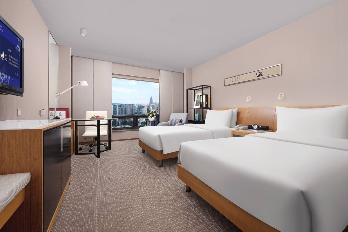 Une chambre d’hôtel avec deux lits, un bureau, une chaise, une télévision et une vue sur la ville.