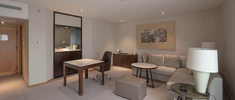 Une chambre d’hôtel moderne avec une porte en bois, un bureau avec une chaise, un canapé, une petite table ronde et une lampe.