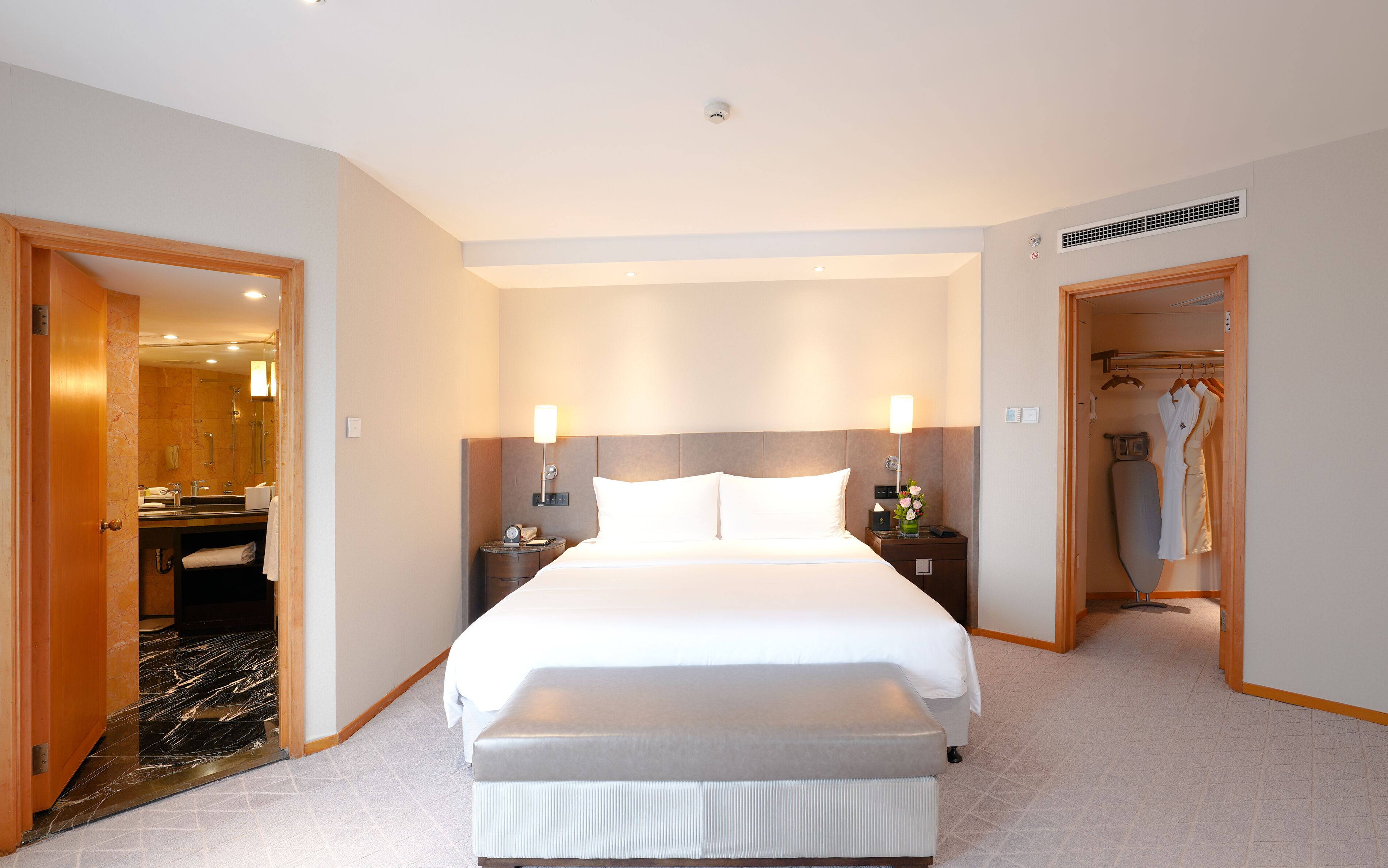 Une chambre d’hôtel dotée d’un grand lit, de deux tables de chevet, d’un miroir, d’un espace douche et d’un dressing avec des peignoirs.