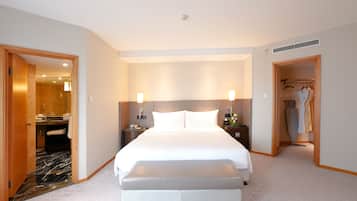 A hotel room with a large bed, two bedside tables, a mirror, a shower area, and a walk-in closet with robes.