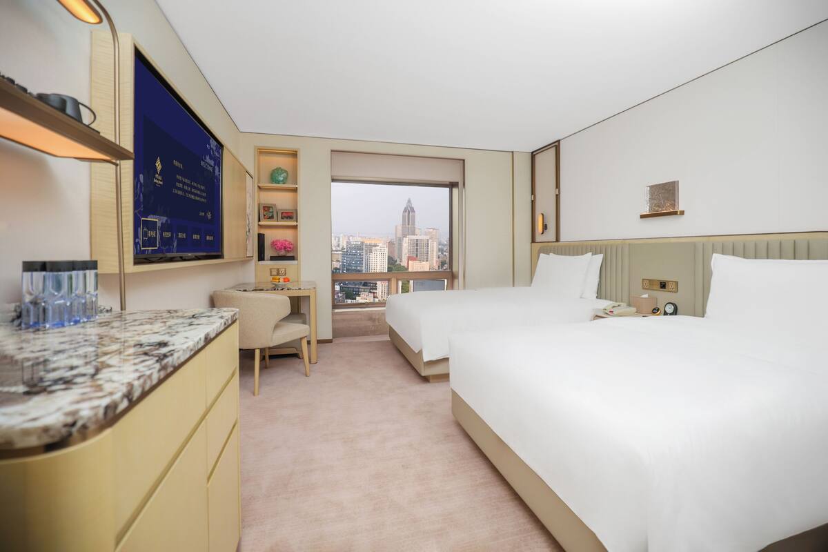 Une chambre d’hôtel équipée d’un lit, d’un bureau, d’une chaise, d’une télévision et d’une fenêtre donnant sur la ville.