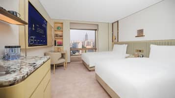 Quarto de hotel com cama, escrivaninha, cadeira, televisão e janela com vista para a cidade.