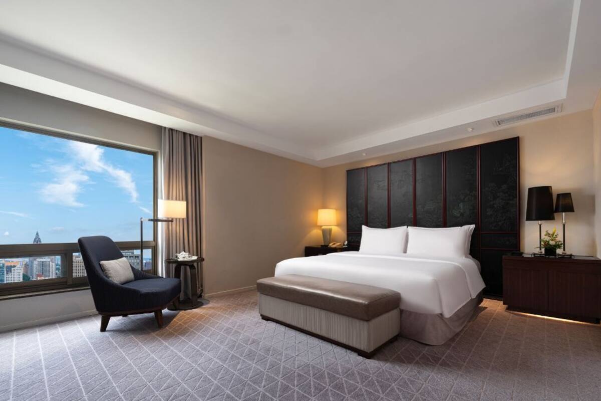 Une chambre d’hôtel avec un grand lit, une chaise, une table de chevet, une lampe et une vue sur la ville.