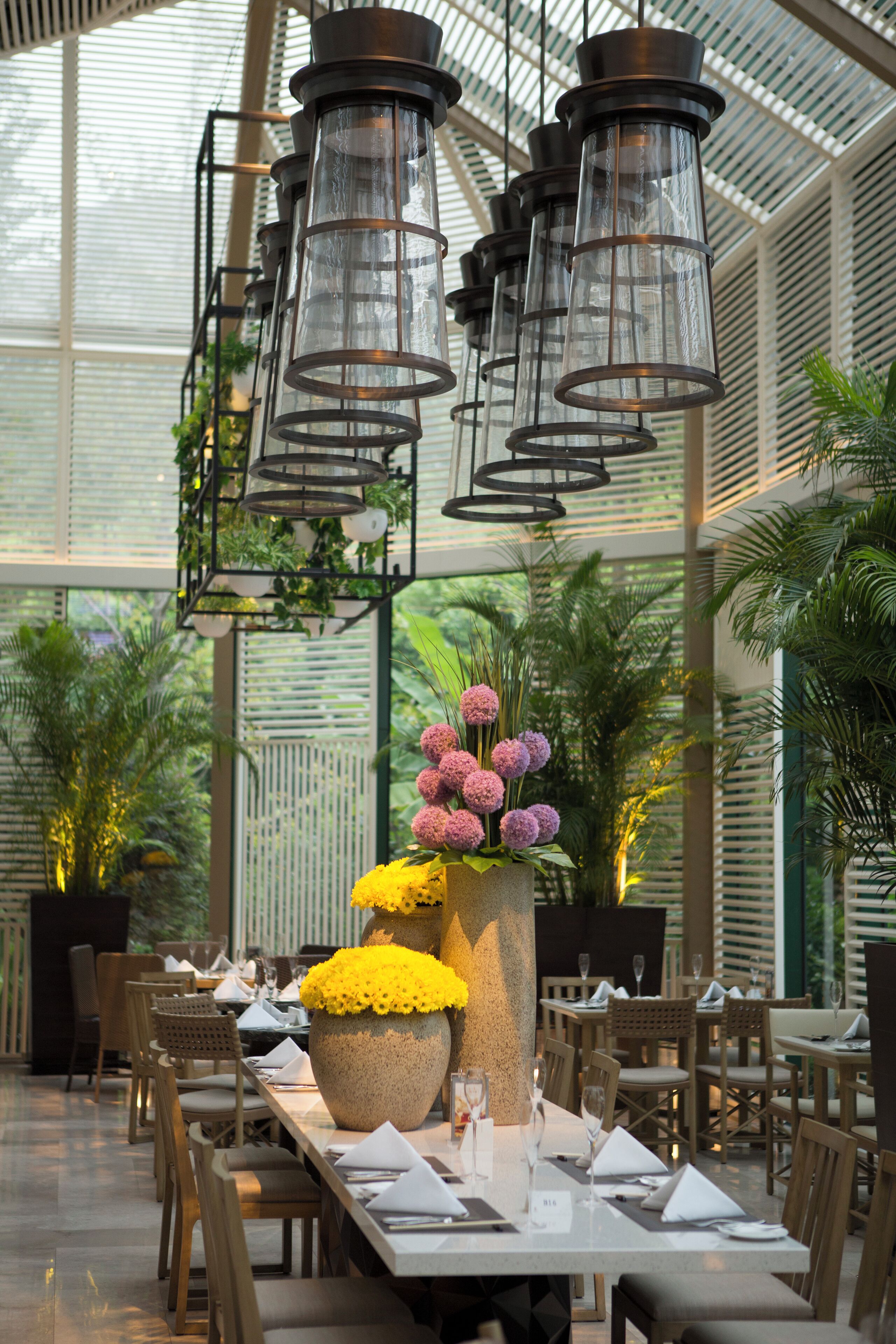 A restaurant with a long table set for dining, hanging lanterns, and potted plants.
