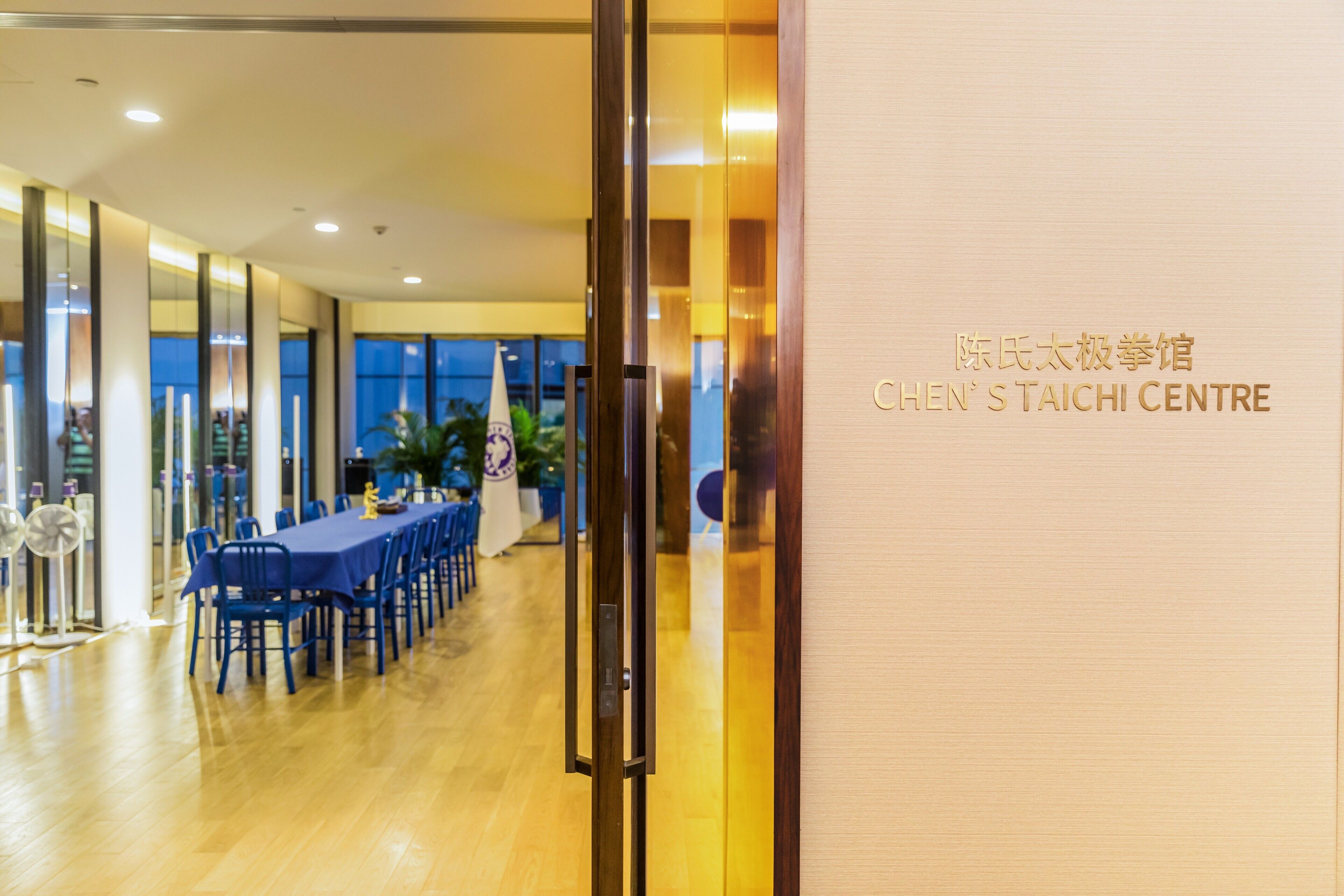 A conference room with a long table and chairs, a wooden floor, and a glass partition.