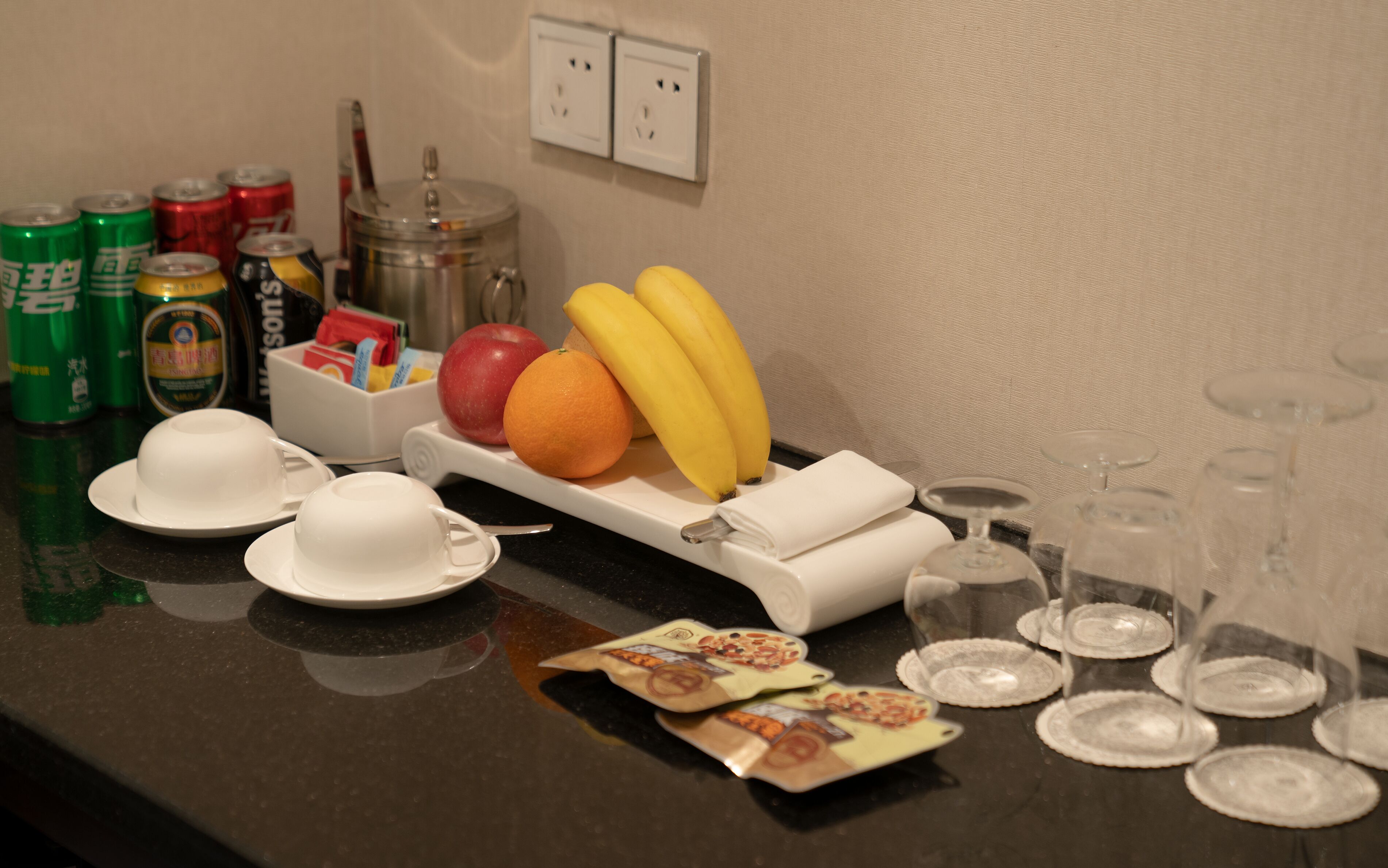 A breakfast setup with plates, cups, a fruit tray, and empty wine glasses.