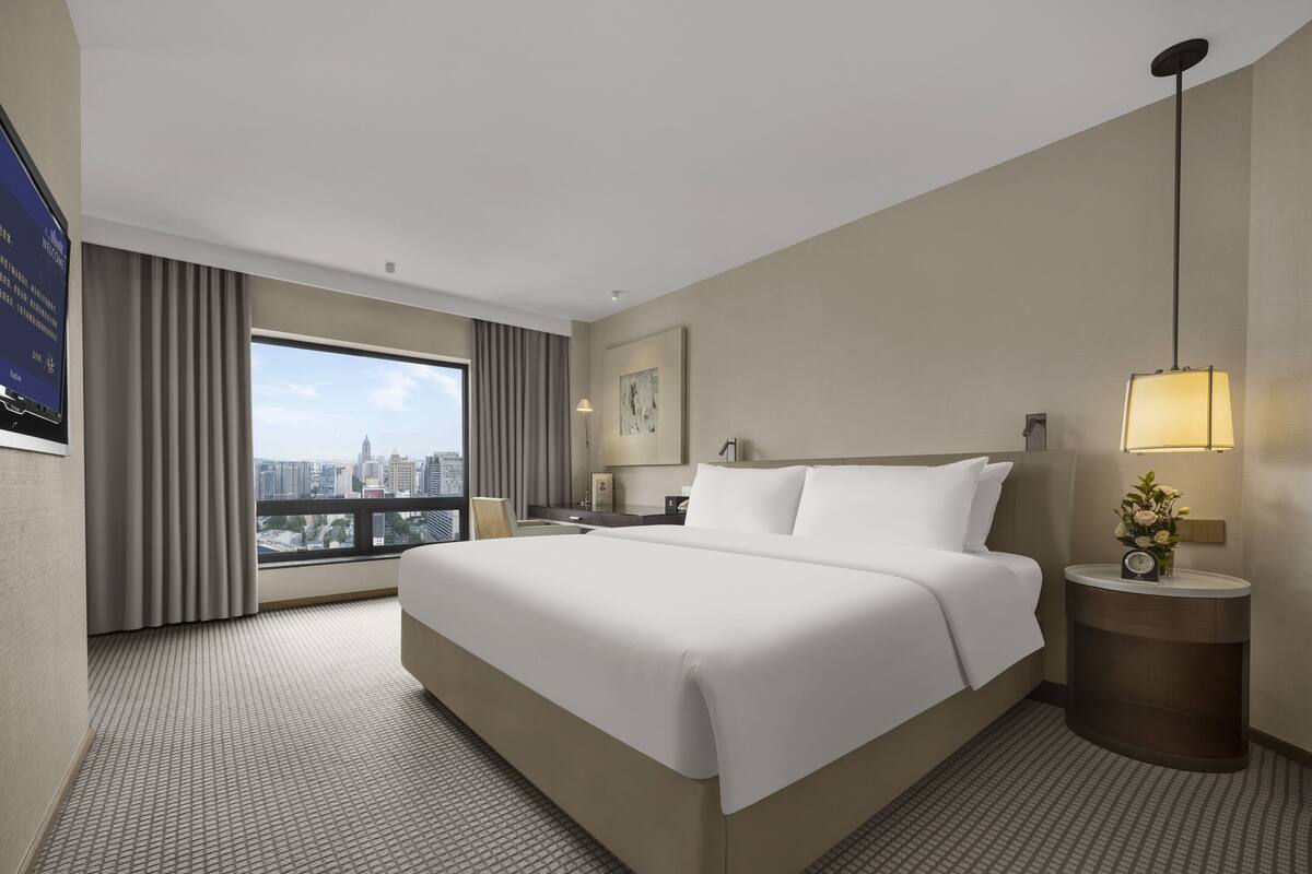 Une chambre d’hôtel avec un grand lit, une table de chevet, une lampe et une vue sur la ville.