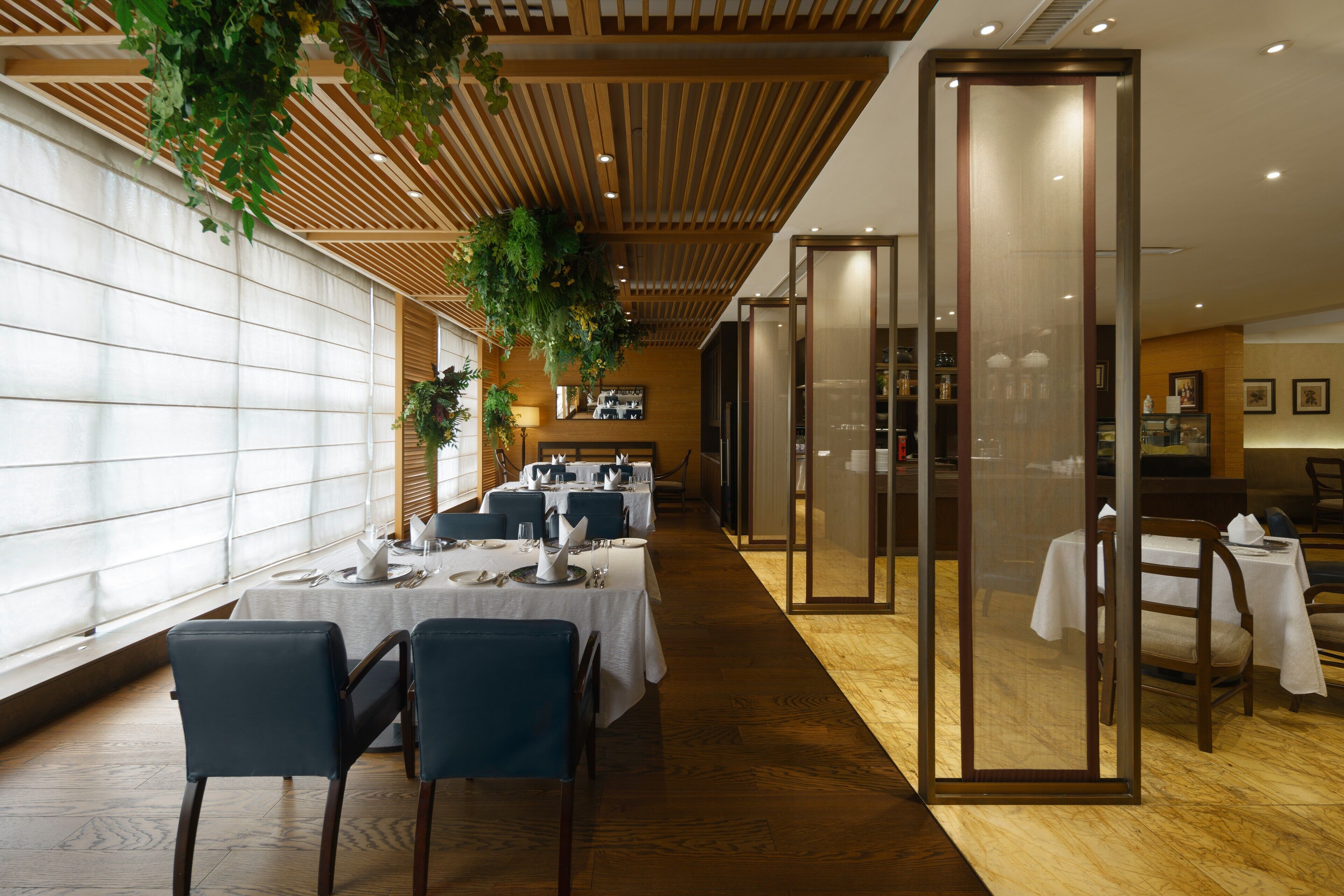 A restaurant with tables set for dining, wooden ceiling, and hanging plants.
