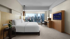 Habitación de hotel con una cama grande, un escritorio, un televisor y vistas a la ciudad.