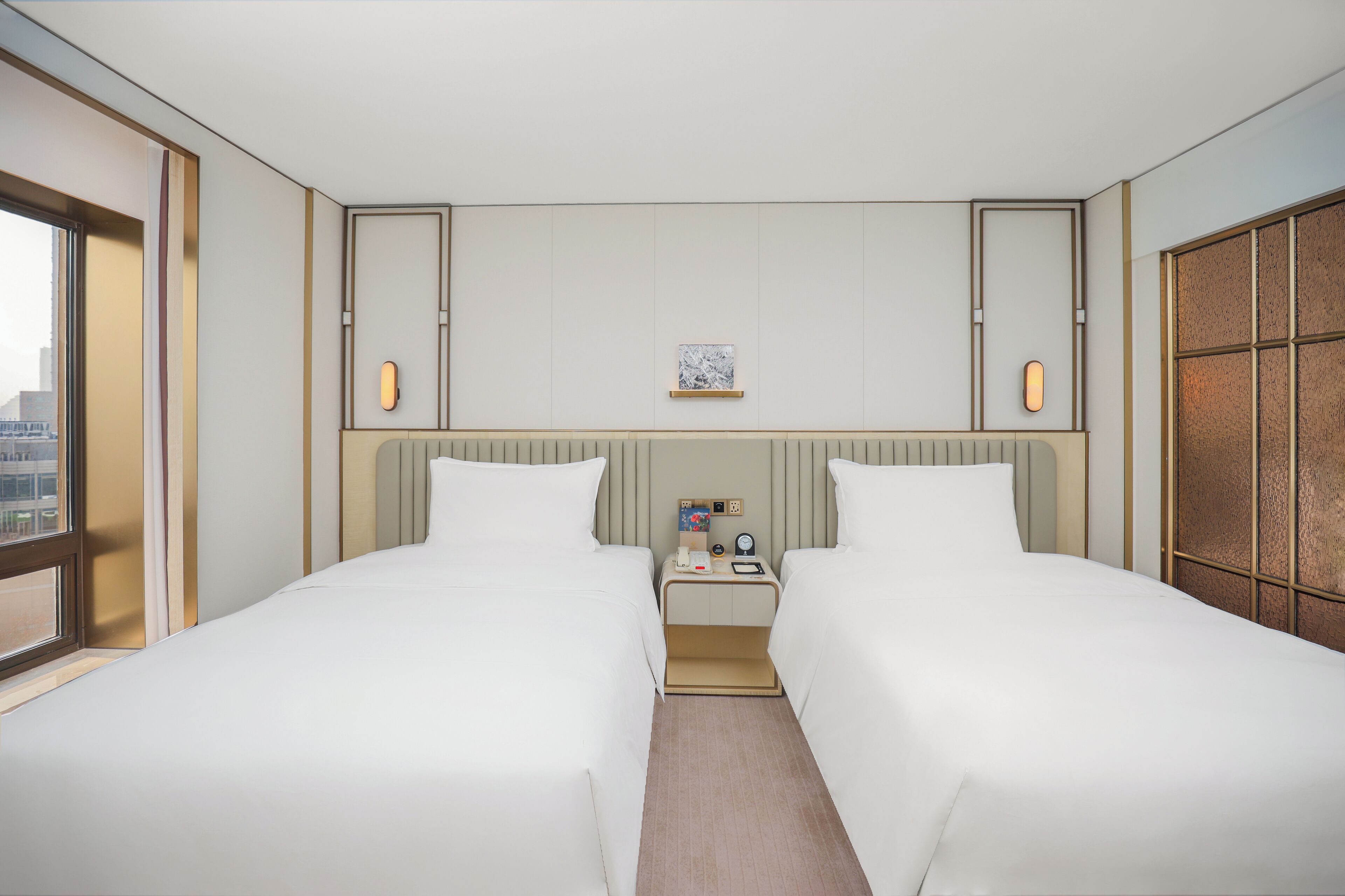 A hotel room with two beds, a nightstand, a small table, and a window.