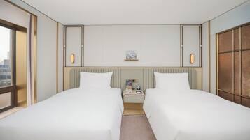 A hotel room with two beds, a nightstand, a small table, and a window.