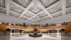 Un vestíbulo amplio con techo alto que presenta patrones geométricos, una escultura central y un piso de mármol pulido.