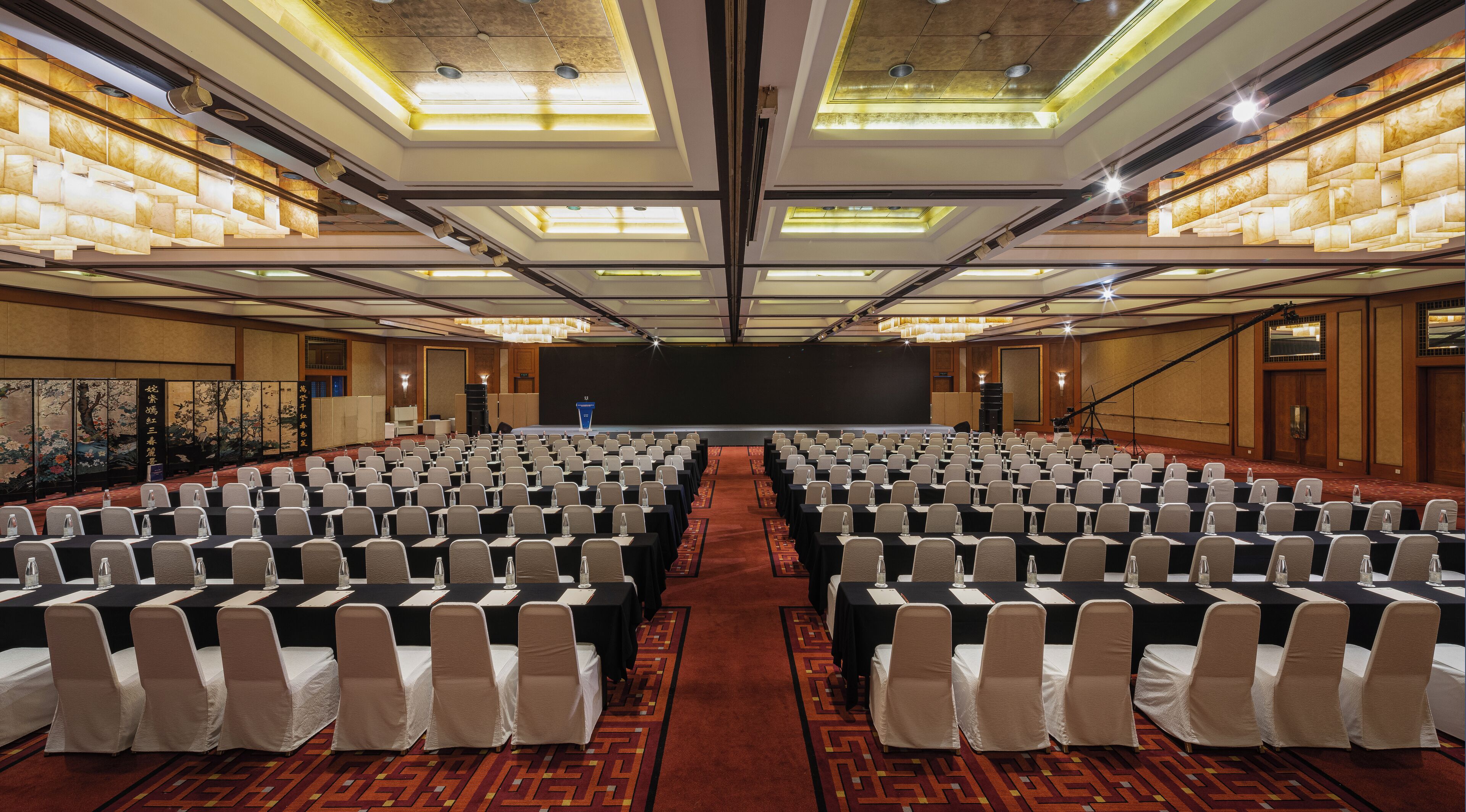 A conference room with rows of chairs, a stage, and a large screen.