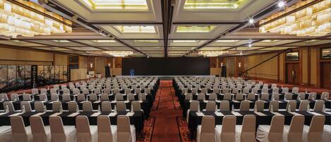 A conference room with rows of chairs, a stage, and a large screen.