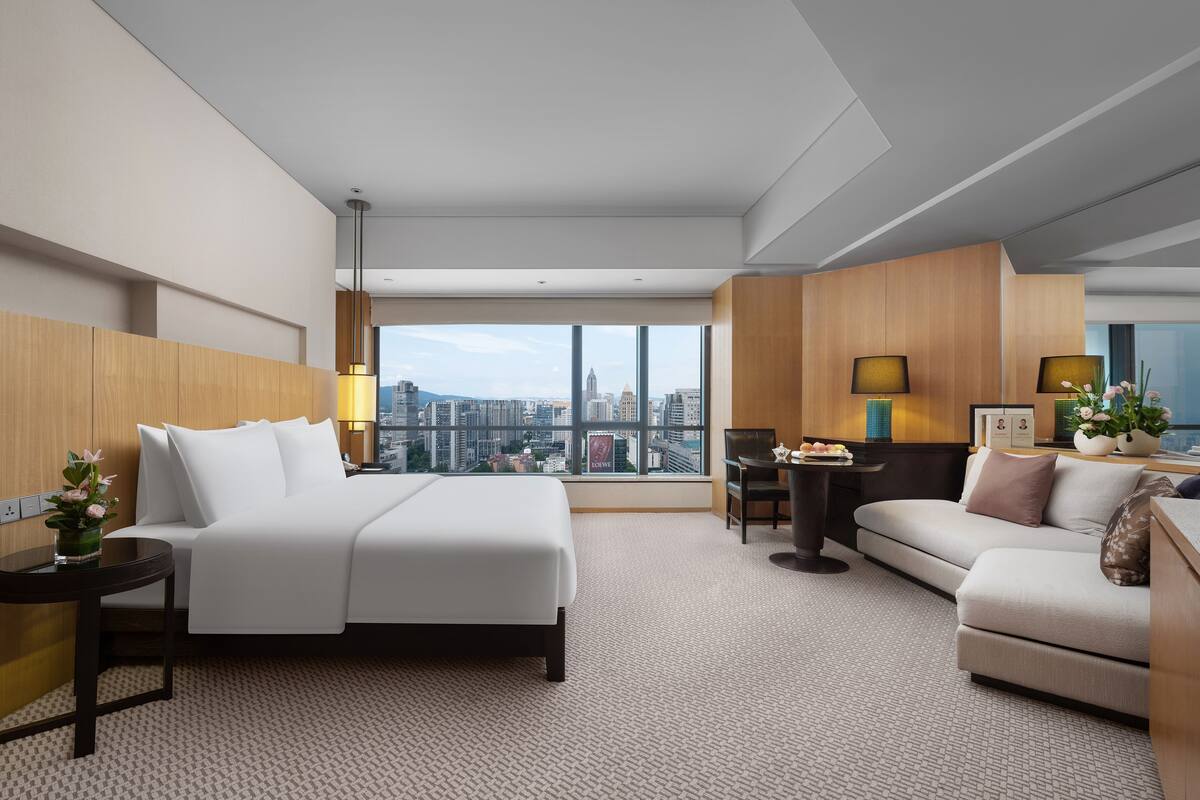 Une chambre d’hôtel moderne dotée d’un grand lit, d’un canapé, d’un bureau et offrant une vue sur le paysage urbain.