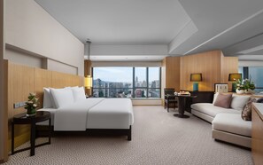 Relax in a spacious room with a large bed and city view, featuring a sofa, table, and decorative vase with flowers.