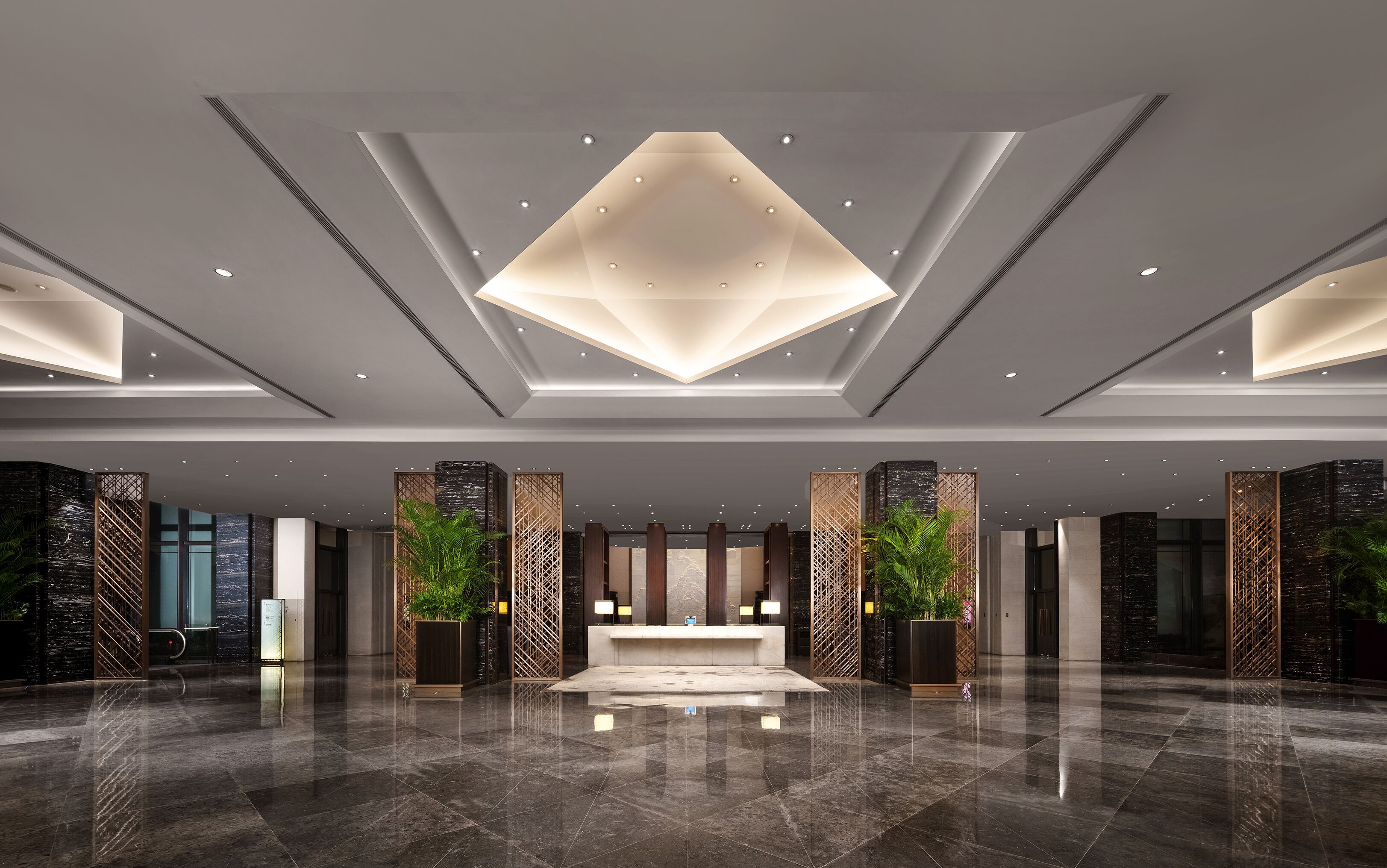 A modern lobby with a reception desk, decorative panels, and a geometric light fixture.