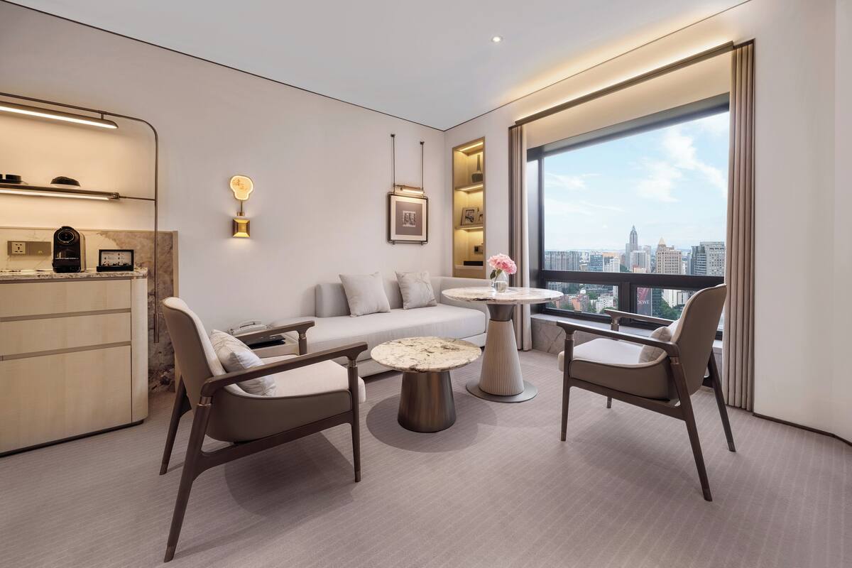 Un salon moderne comprenant un canapé, deux fauteuils, une table basse et une vue sur la ville grâce à de grandes fenêtres.
