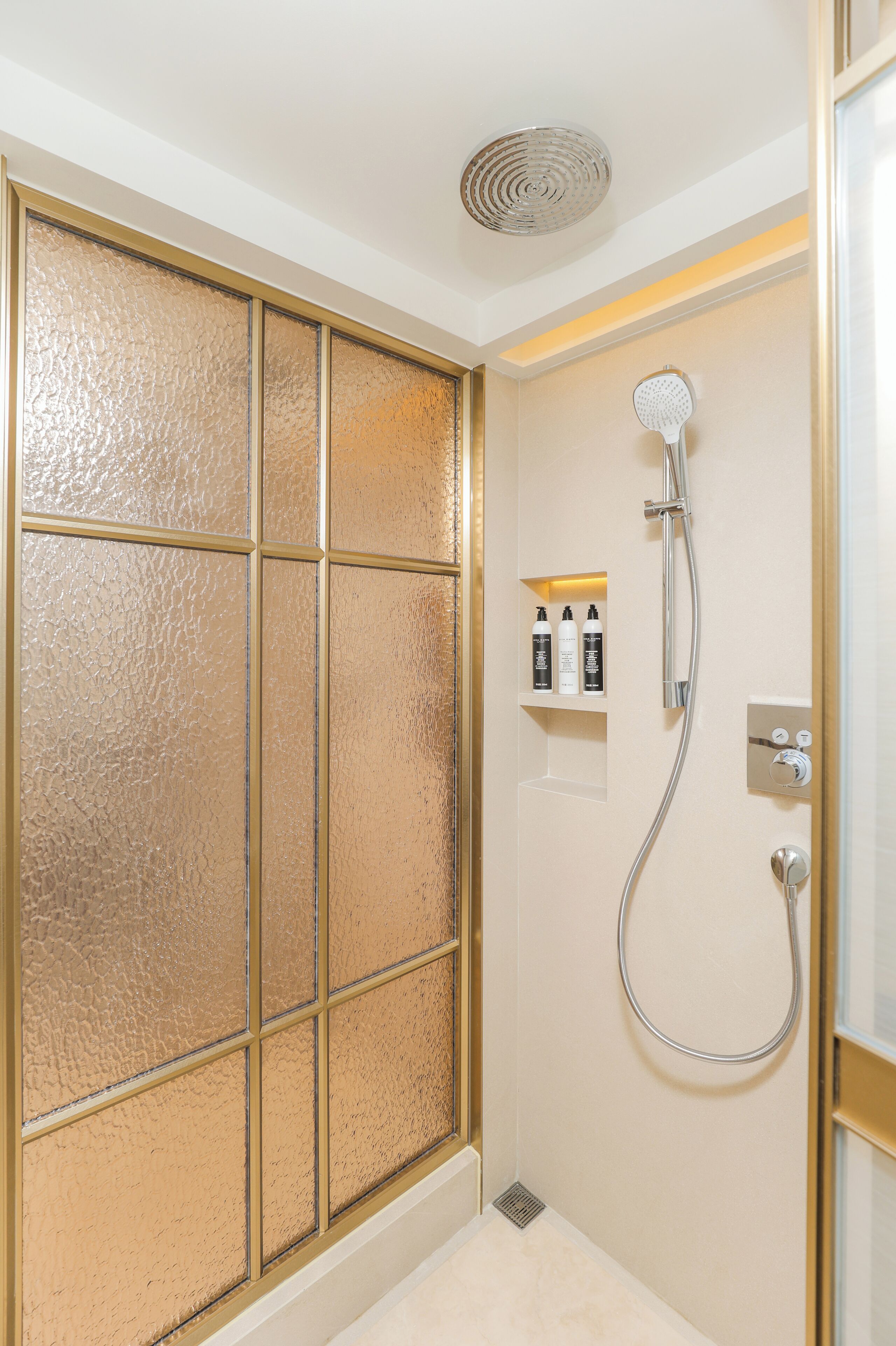 Ein Badezimmer mit Glastrennwand, einer Dusche inklusive Handbrause und Ablagefläche für Toilettenartikel.