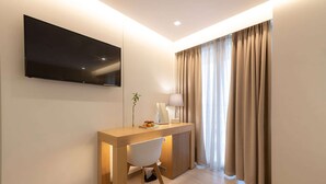 Habitació d'hotel moderna amb un televisor de pantalla plana fixat a la paret, un escriptori de fusta amb una cadira, una làmpada i una planta.