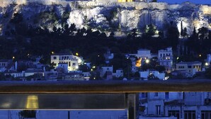 Taula per a dues persones amb ampolla de vi, un got i una planta en test, amb vista a un paisatge urbà i un edifici històric al fons.