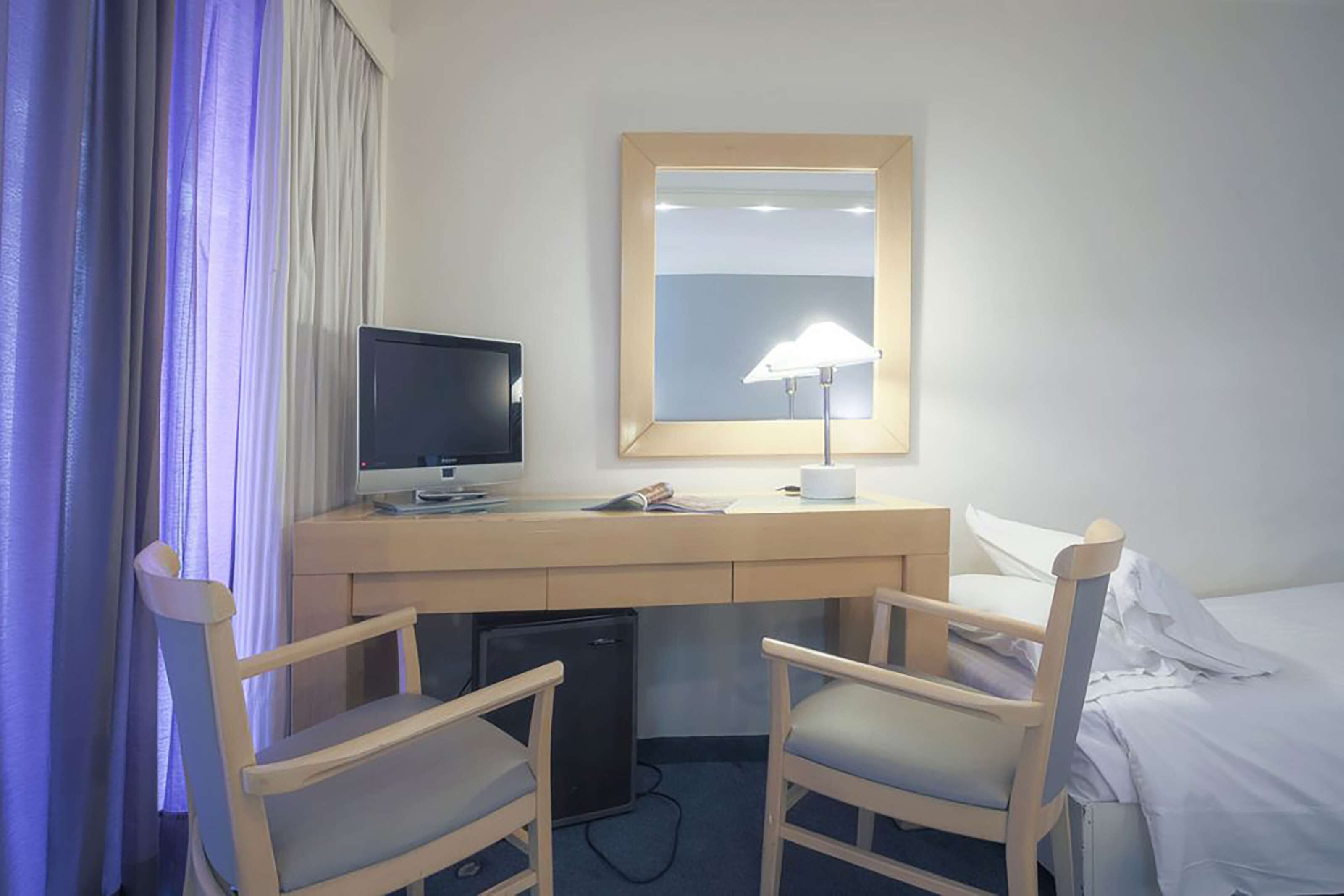 Habitación de hotel con escritorio, dos sillas, cama, televisor y espejo.