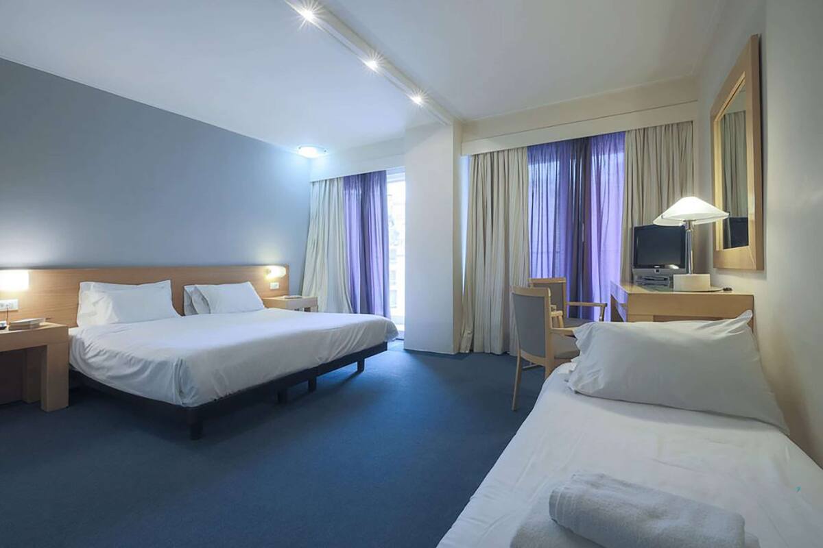 A hotel room with two beds, a desk, a chair, a TV, and a lamp.
