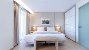 Habitació d'hotel moderna amb un llit gran, làmpades de nit, una obra d'art emmarcada a la paret i una tauleta de nit de fusta.