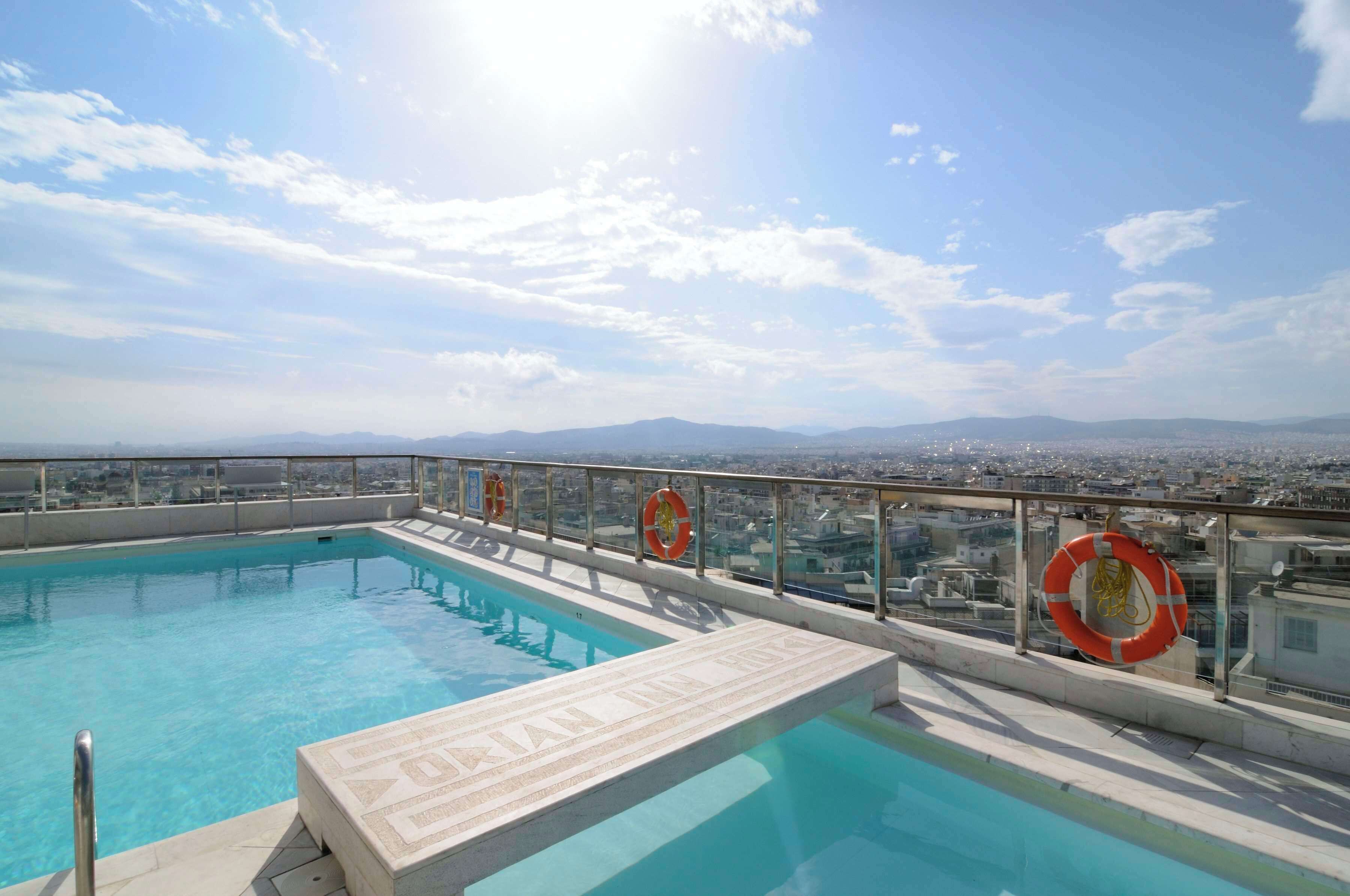 A rooftop pool with clear blue water, surrounded by a glass railing and lifebuoys.